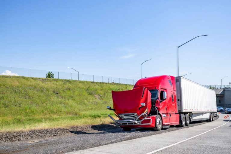 A red semi truck stopped on the highway shoulder with its hood open, waiting for roadside repair